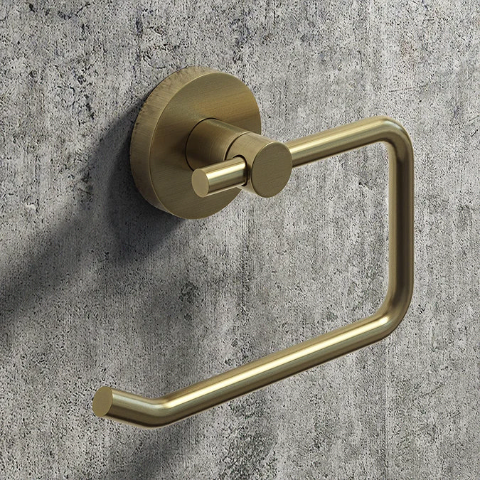 Wall-mounted brushed brass toilet roll holder with a minimalist, industrial design, set against a textured grey concrete wall.