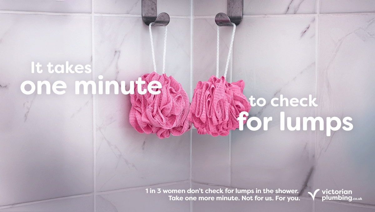 Two pink shower poufs hanging on hooks against a marble-tiled shower wall. Overlay text reads: It takes one minute to check for lumps. Below, smaller text states: 1 in 3 women don’t check for lumps in the shower. Take one more minute. Not for us. For you. Victorian Plumbing logo in the bottom right corner.