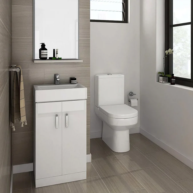 Compact white vanity unit with sink and storage next to a close-coupled toilet in a modern bathroom with neutral beige tiles