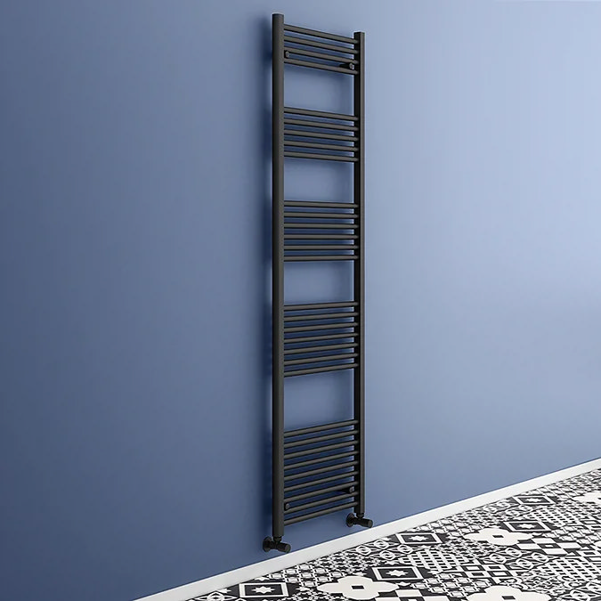 Tall matt black Toreno towel radiator mounted on a blue bathroom wall, paired with patterned monochrome floor tiles for a modern high-contrast look.