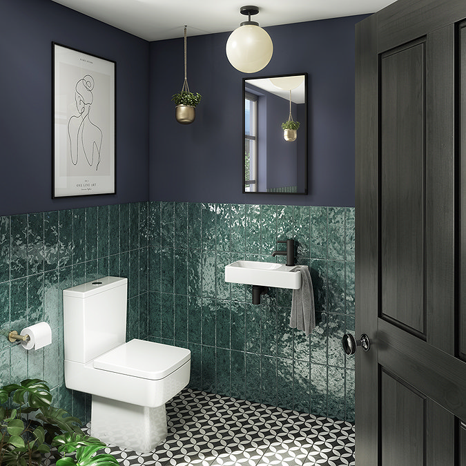 Stylish bathroom with emerald green gloss tiles, geometric floor tiles, and a contemporary white toilet and sink, complemented by a round pendant light and hanging plants.