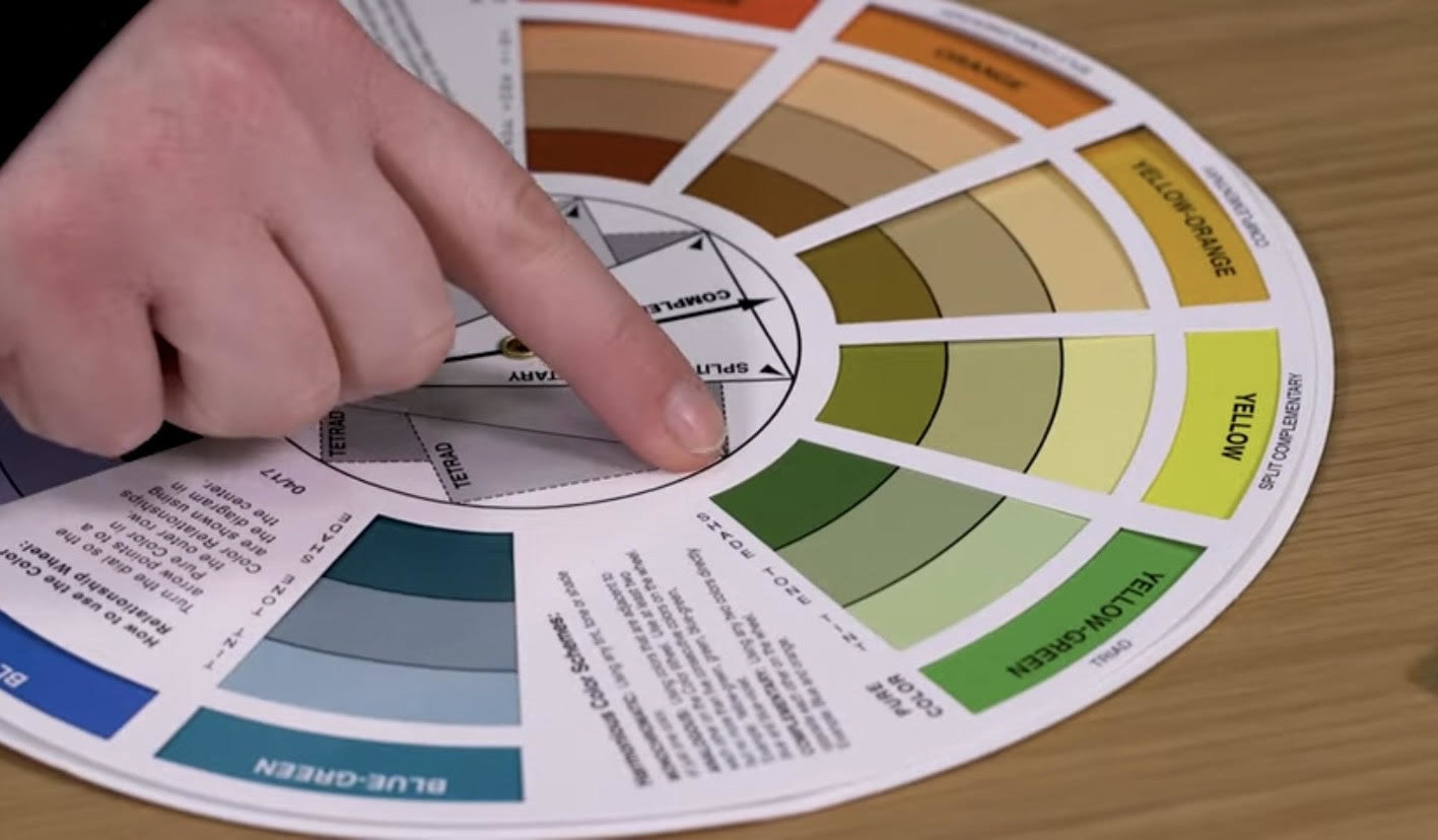 Close-up of a person using a colour wheel to select complementary shades, demonstrating how to create harmonious colour schemes for interior design projects.