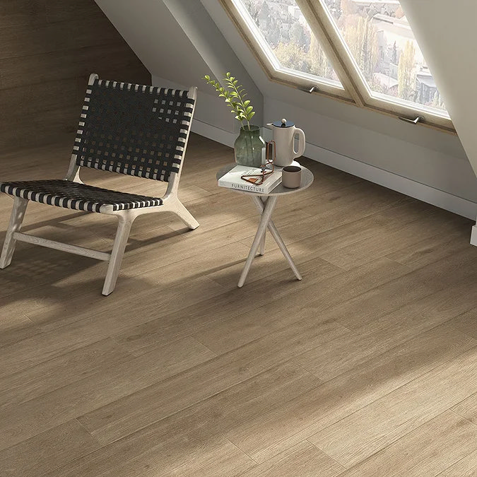 Wood-effect floor tiles in a cosy attic space with a woven chair, side table, and large skylight windows for a warm, natural look.