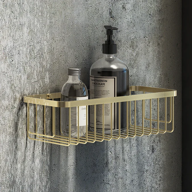 Wall-mounted brushed brass shower basket holding bottles of toiletries, set against a textured grey wall, adding a touch of elegance and functionality to the bathroom decor.