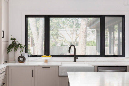 Bright modern kitchen with large black-framed window, farmhouse sink, and minimalist beige cabinetry