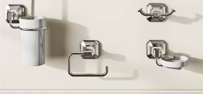 Chrome bathroom accessory set, including a wall-mounted toilet roll holder, toothbrush holder, and soap dish, showcasing a modern and coordinated design against a cream wall.