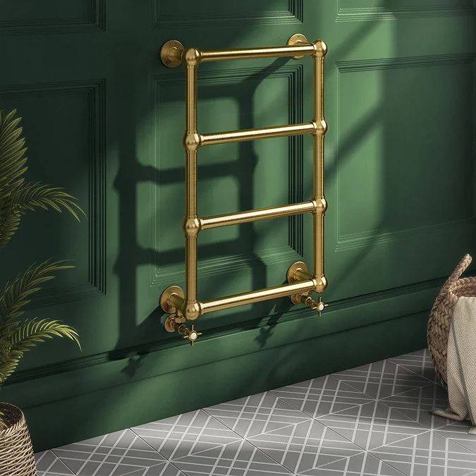 Elegant vintage-style gold towel radiator mounted on a deep green bathroom wall, adding a touch of luxury to the classic bathroom decor.