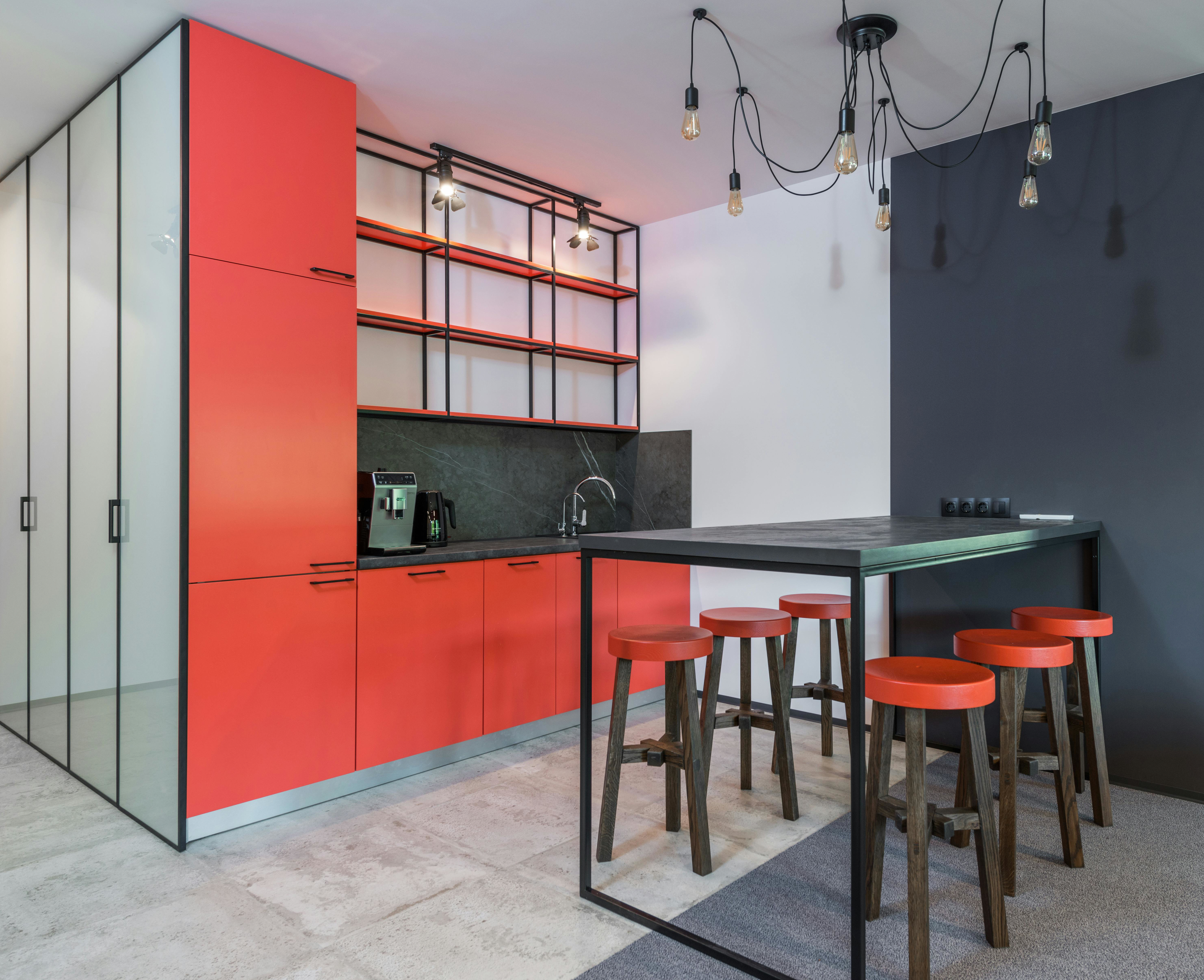 Modern small kitchen with bold red cabinets, open shelving and black breakfast bar with stools, exposed bulb lighting and two-tone walls.