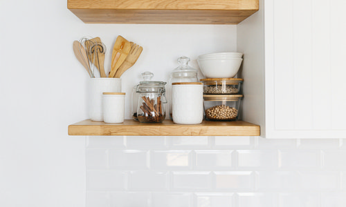 Minimalist white kitchen shelf with wooden accents, glass jars of spices, and neatly stacked bowls