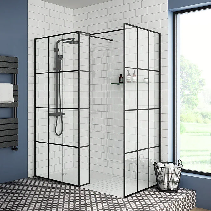 Stylish wet room with a modern industrial look, featuring a black grid-framed glass shower screen, rainfall showerhead, and white metro tiles. The patterned monochrome floor and matte black towel radiator add a striking contrast to the clean, minimalist design.