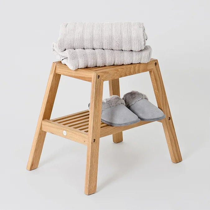 Wooden bathroom stool with folded towels and slippers on lower shelf