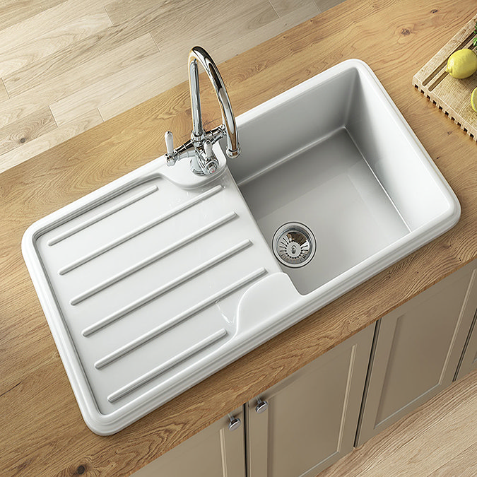 Elegant white ceramic kitchen sink with a drainer and chrome mixer tap, set into a wood countertop with beige cabinets.