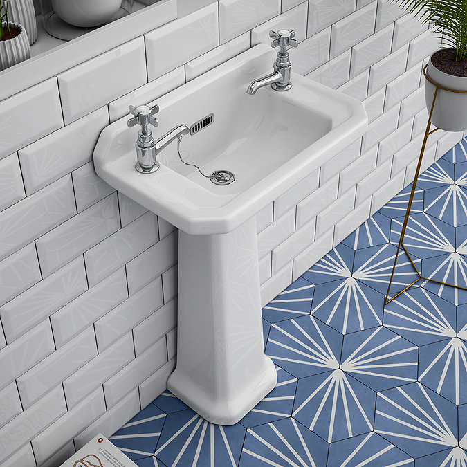 Traditional white pedestal basin with dual taps against white subway tiles and blue patterned floor.