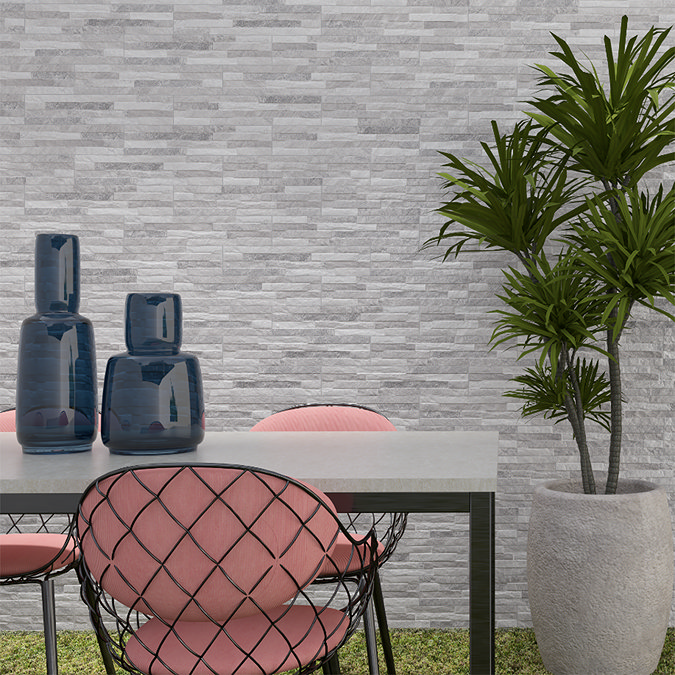 Outdoor feature wall clad in light grey split-face stone tiles behind a modern garden dining set – Casterton Split Face Light Grey.