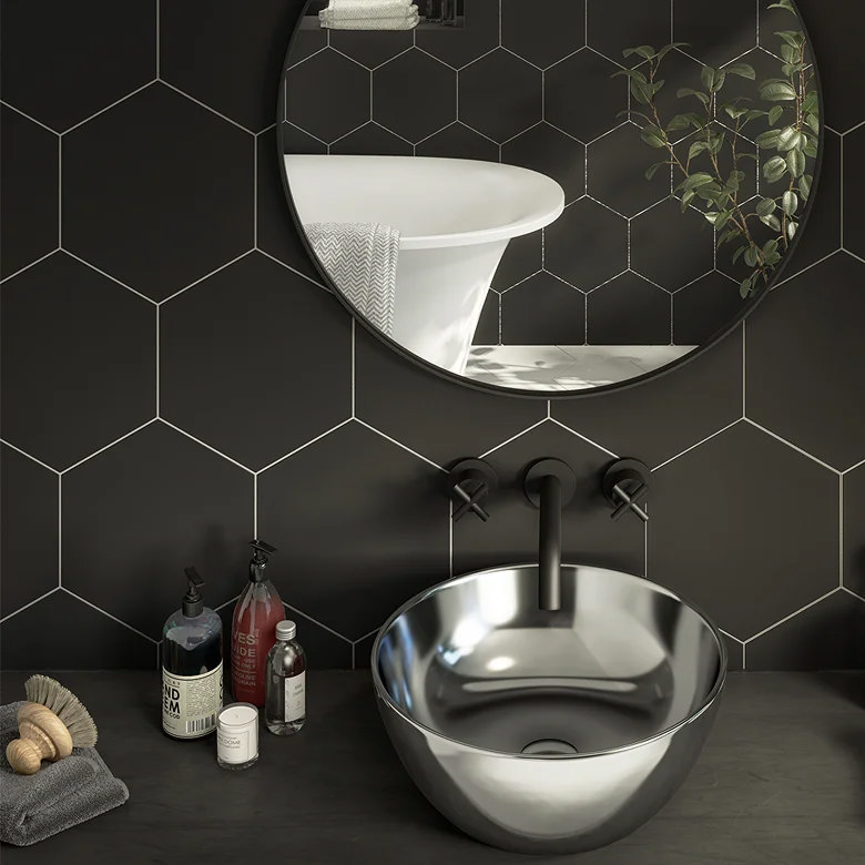 Black hexagon bathroom wall tiles behind a round mirror and metallic countertop basin.