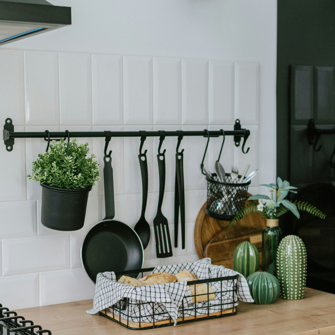Modern kitchen counter with wall-mounted black utensil rack, potted plant, and wire bread basket
