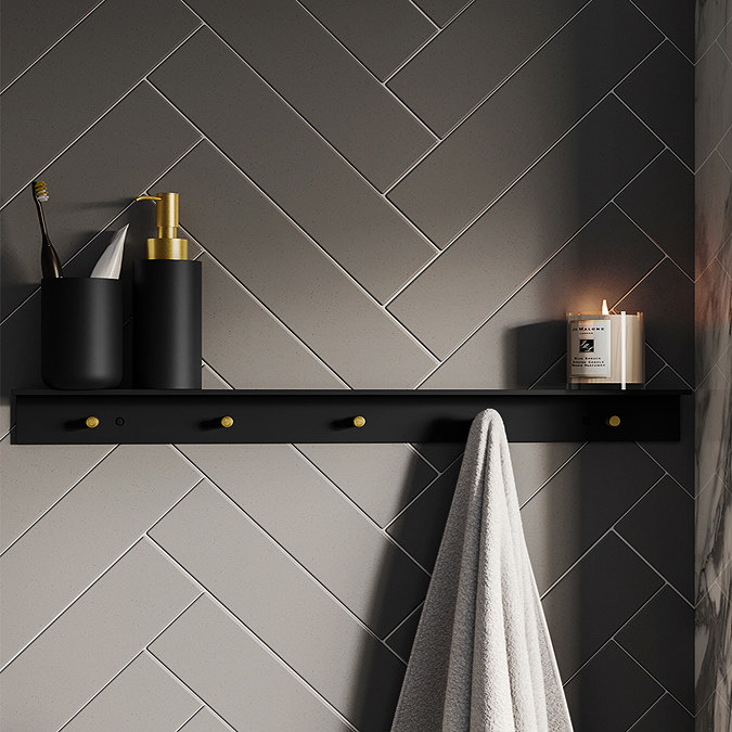 Black bathroom shelf with gold hooks holding towel, toothbrush holder and candle