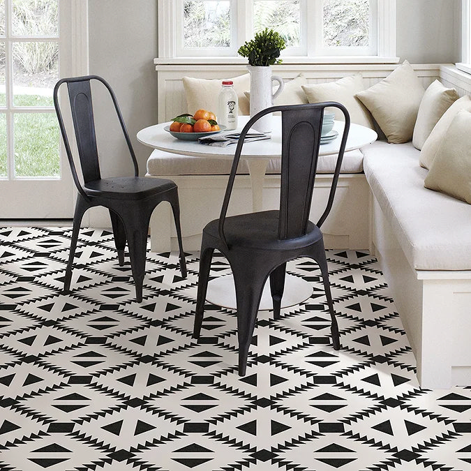 Bold black and white geometric pattern floor tiles in a cosy dining nook with metal chairs, a round table, and built-in seating by a large window.