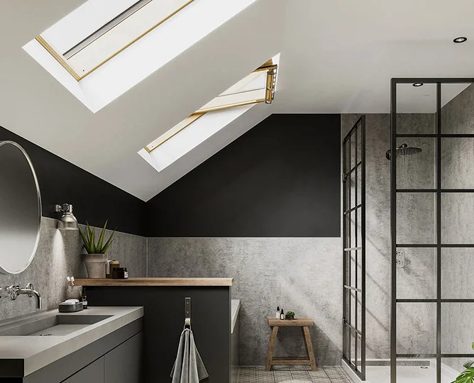 Modern loft bathroom with a sloped ceiling and skylights, featuring a walk-in shower with black-framed glass panels, grey textured walls, and a dark vanity unit with a wooden countertop. Includes a minimalist stool and potted plants for a natural touch.