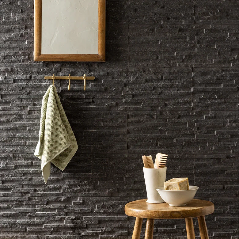 Black split face stone bathroom wall with textured tiles and wooden accessories.