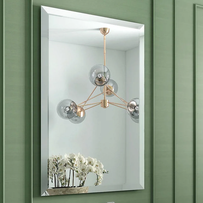 Modern bathroom mirror reflecting a gold chandelier with glass globes and a vase of white orchids, set against a green wall panel.