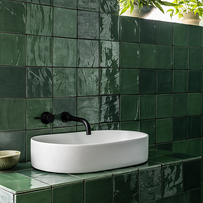 Glossy green wall tiles with a sleek white countertop basin and black wall-mounted tap, adding a vibrant and modern touch to the bathroom.