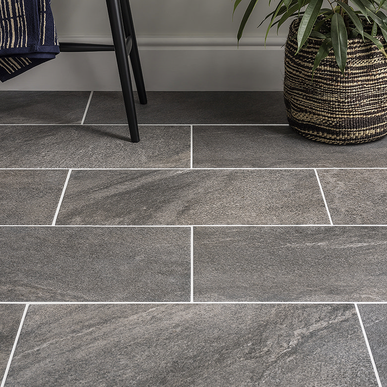 Grey textured floor tiles styled with a plant basket and black chair.