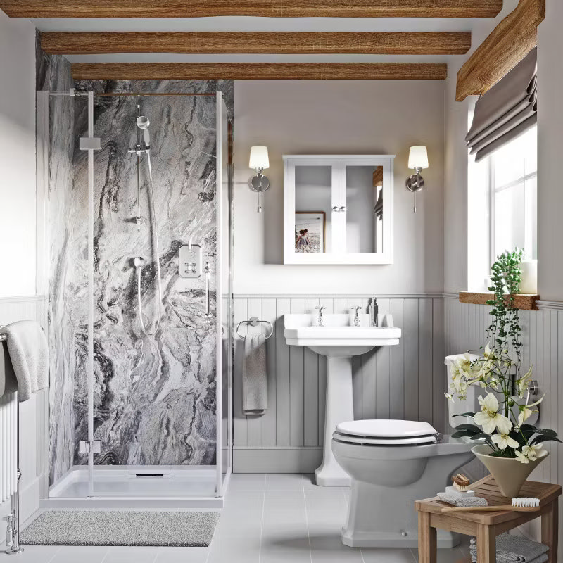 Rustic bathroom featuring a marble-effect shower, exposed wooden beams, and soft grey panelling. Includes a pedestal sink, traditional toilet, and elegant wall lighting for a cosy, classic feel.