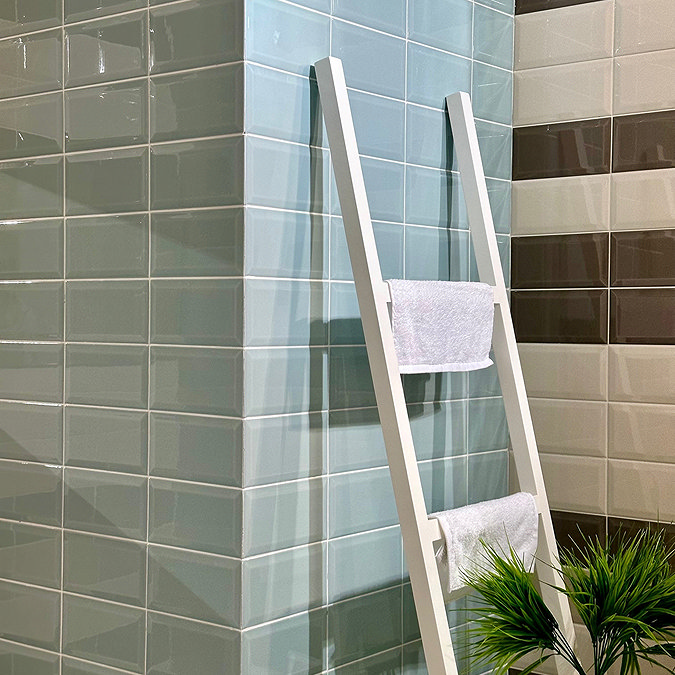 Glossy pastel green and beige metro tiles used in a modern bathroom, styled with a white ladder towel rack and a potted plant for a fresh and clean aesthetic.