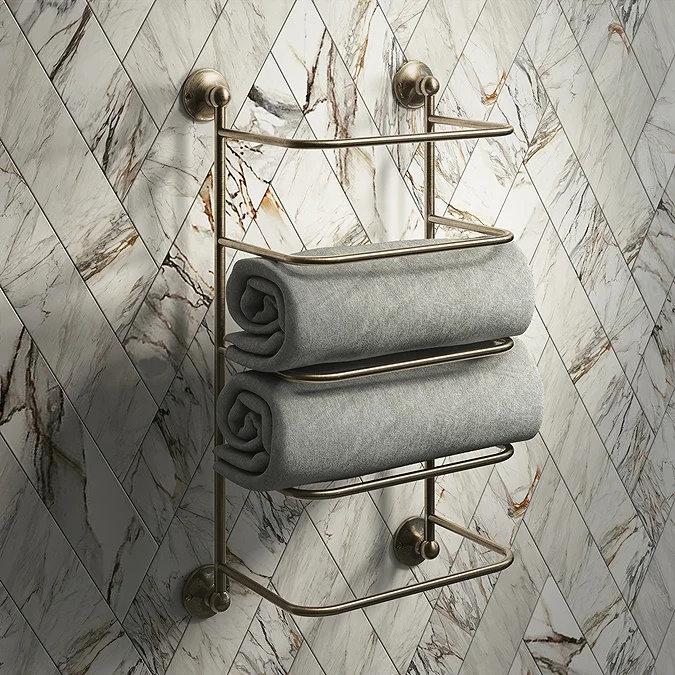 Wall-mounted bronze towel stacker holding two neatly rolled grey towels in a marble bathroom
