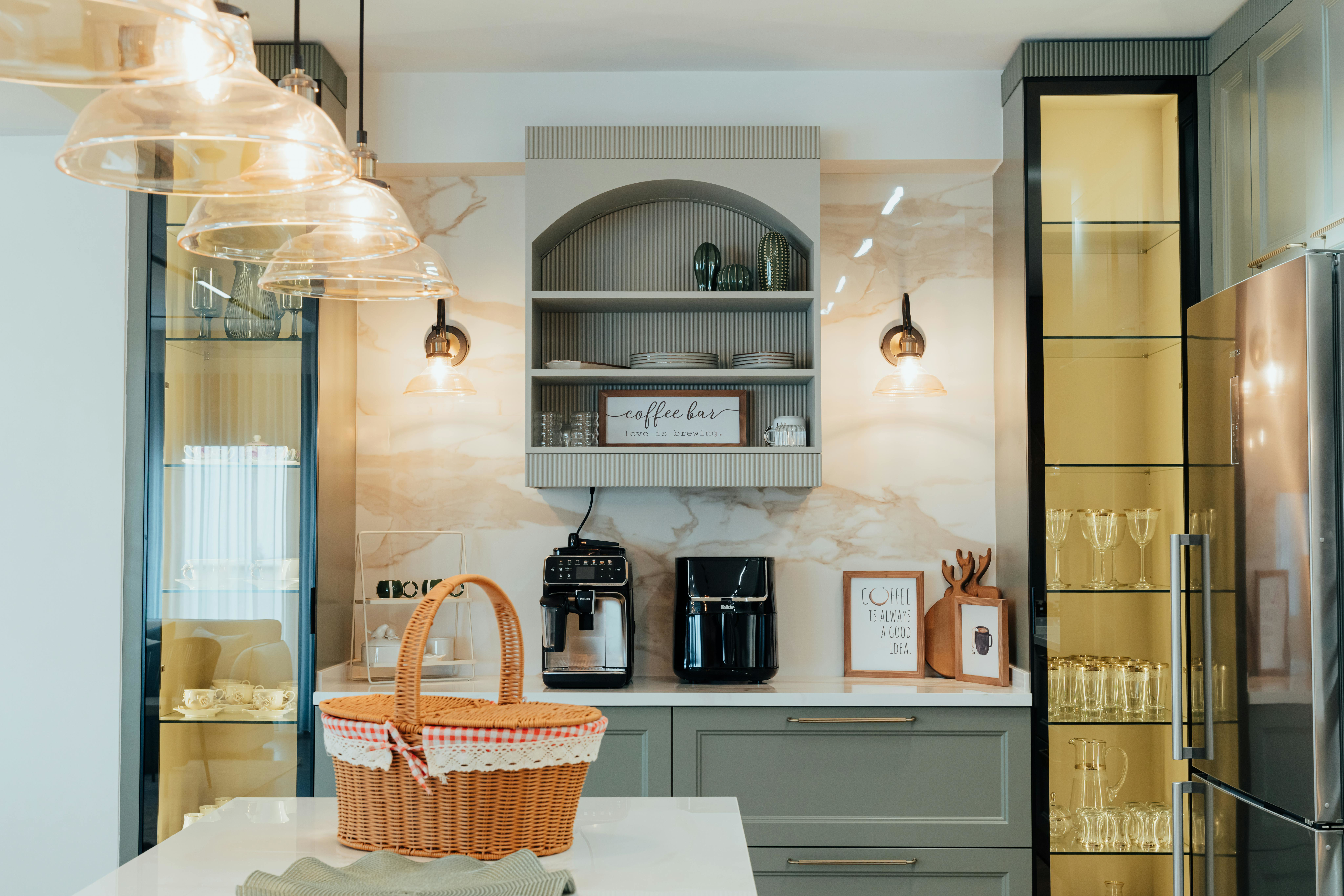 Compact kitchen with sage-green cabinets, arched open-shelf coffee bar, marble splashback, glass display cabinets and pendant lighting.
