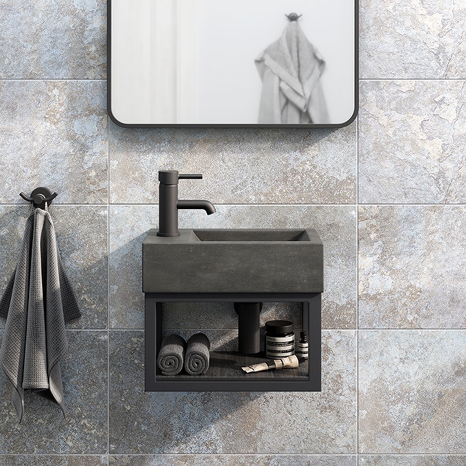 Compact wall-mounted cloakroom basin with black frame and storage shelf against grey textured tiles