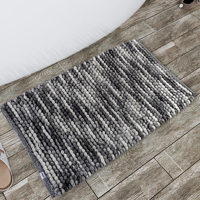 Soft grey and white textured bath mat placed on wood-effect bathroom flooring, adding comfort and style to the space. The mat’s woven pattern complements the rustic floor tiles, providing a cosy, functional addition next to the bathtub.