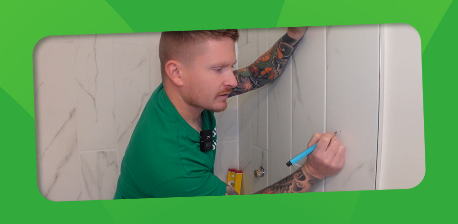 Man marking a tile with a pencil in a bathroom, preparing to drill, as part of a Victorian Plumbing guide on how to drill through tiles.