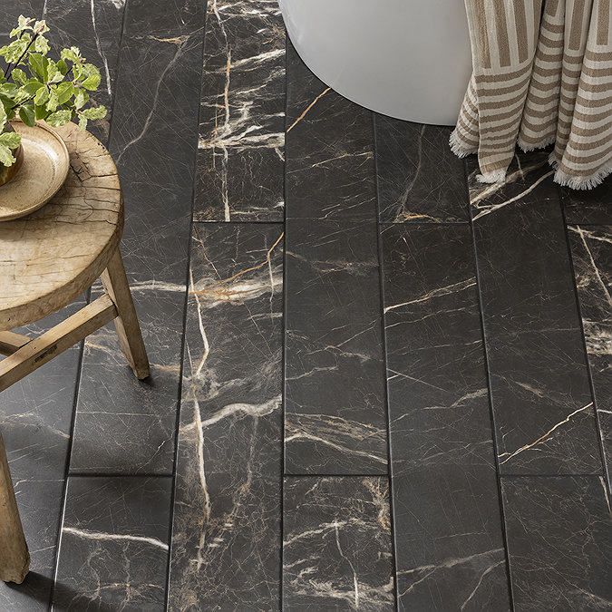 Dark wood-effect bathroom floor tiles with a rich, marble-like veining pattern, paired with a rustic wooden stool and striped beige towel. The luxurious design creates a sophisticated yet natural look.