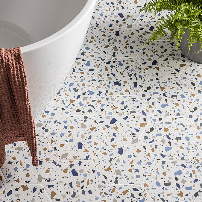 Colourful terrazzo hexagon floor tiles in a bathroom with a white bathtub, pink towel, and a green potted fern for a vibrant, modern look.