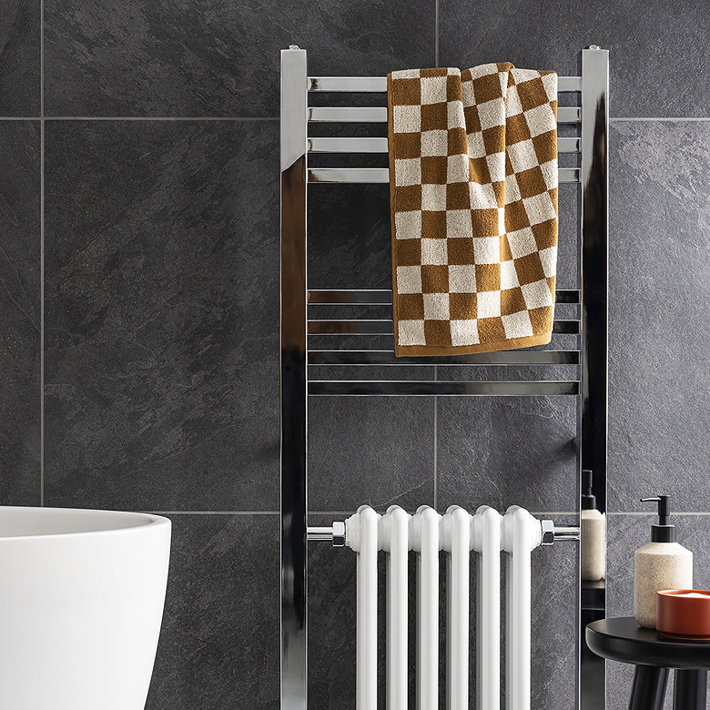 Chrome towel radiator against dark stone-effect bathroom tiles.