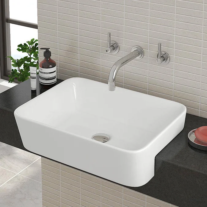 White semi-recessed rectangular basin with wall-mounted chrome tap on a dark countertop.