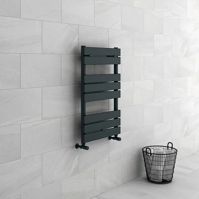 Modern anthracite towel radiator mounted on light stone-effect tiles, adding a sleek and functional touch to the bathroom, paired with a minimalist black wire basket.