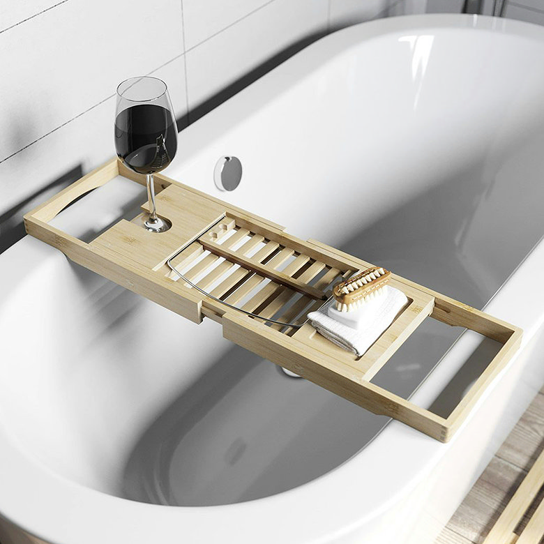 Adjustable wooden bath caddy tray across a white bath for keeping drinks, toiletries and bathing essentials within reach