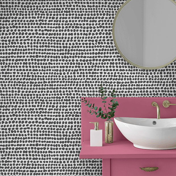 Black and white wallpaper with pink vanity unit and brass tap