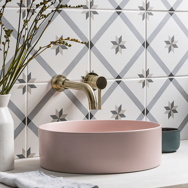 Pastel pink basin with brass taps and grey tiles