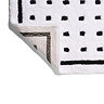 The bottom corner of the Croydex White and Black Squares Bath Mat flipped up showing the anti-slip feature on the underside, pictured on a white background.
