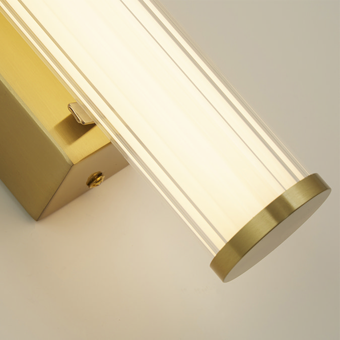 Close‑up of the clamp wall light showing the ribbed opal glass tube softly glowing against the gold backplate