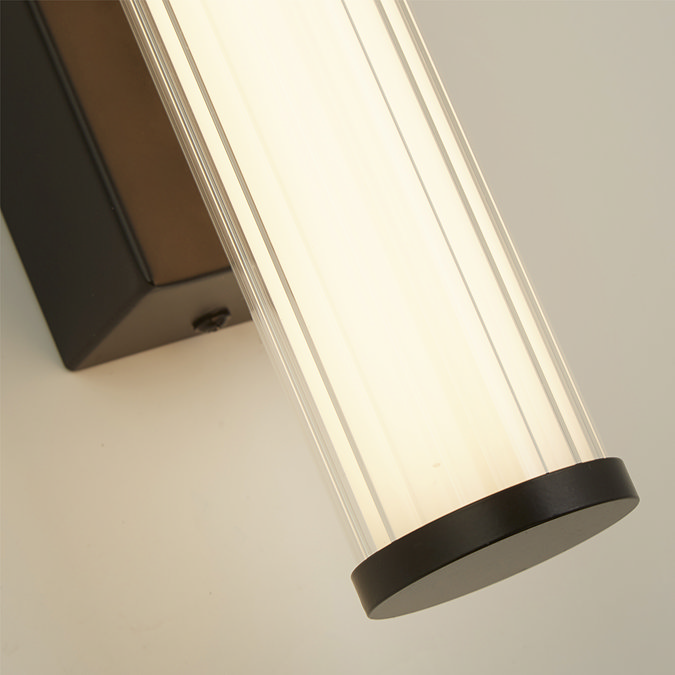 Close‑up of the matt black clamp wall light showing the ribbed opal glass tube softly glowing against the matt black backplate. 