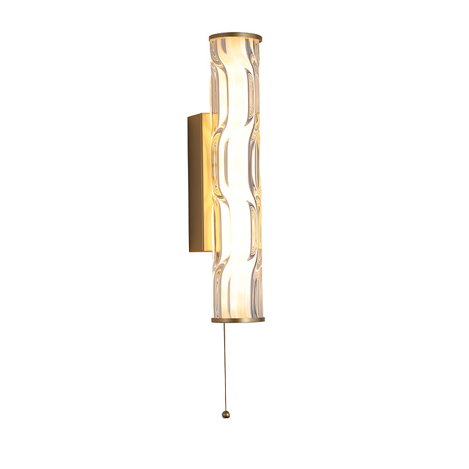A tall matt gold wall light with a glowing wave‑ridged glass diffuser and a pull‑cord hanging from the bottom.