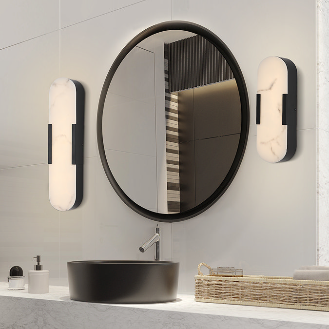 Modern bathroom interior with a large round mirror above a countertop basin, flanked on both sides by differing sized matte‑black wall lights with softly glowing marble‑effect diffusers.