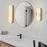 Modern bathroom with a round mirror above a countertop sink, flanked by two wall‑mounted lights featuring glowing oval marble‑effect diffusers framed in matte gold.
