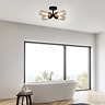 A matt black four‑light flush ceiling fixture with ribbed glass shades mounted in a modern bathroom above a freestanding bath, softly illuminating a bright space with large windows.