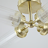 Close‑up of a satin brass ceiling light showing the central round fitting and four ribbed clear glass shades extending outward in a cross shape.